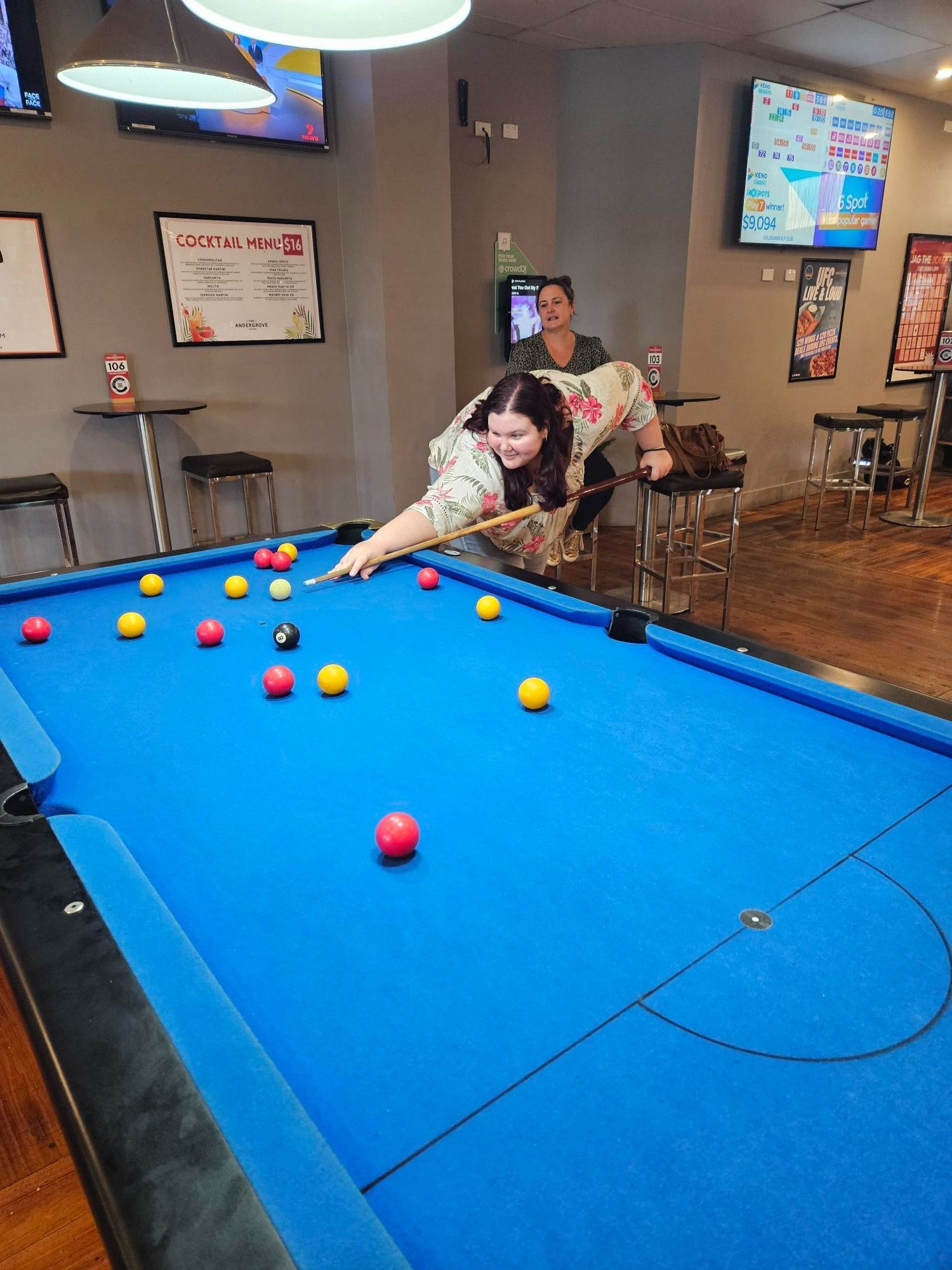 A Person Leaning Over A Bright Blue Pool Table To Take A Shot, With A Bar Setting In The Background — Advanced Therapy Mackay In Mackay, QLD 