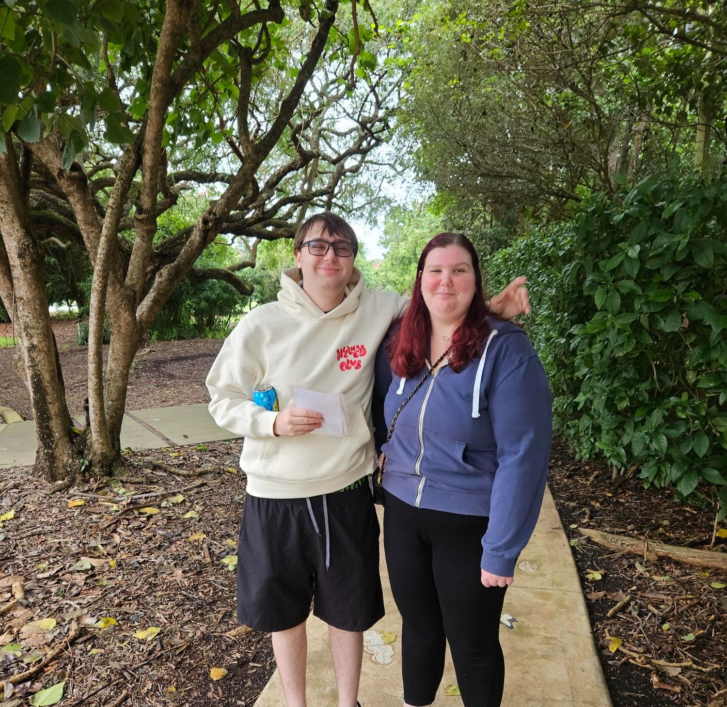 Two People Standing Together Outdoors On A Paved Path Surrounded By Trees And Greenery, Both Smiling At The Camera — Advanced Therapy Mackay In Mackay, QLD 