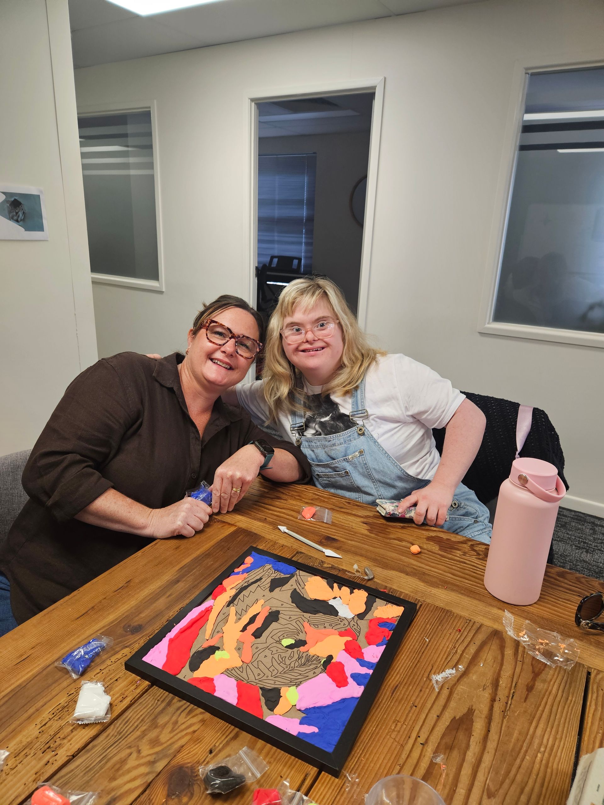 Two people sitting at a wooden table, smiling while working on a colorful mosaic craft project in a brightly lit room — Advanced Therapy Mackay In Mackay, QLD 