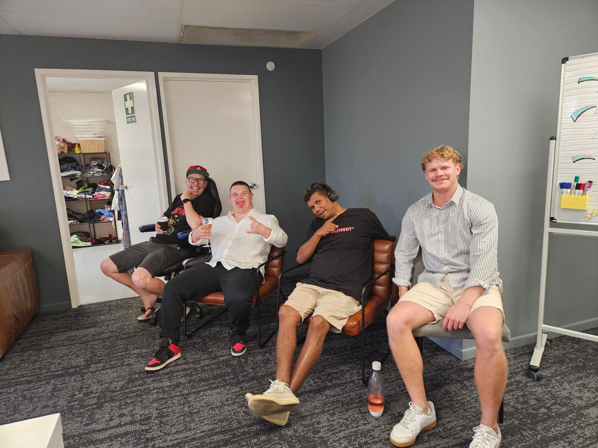 Four People Sit In Chairs In An Office, Smiling And Posing For A Photo In Front Of A Whiteboard And An Open Door — Advanced Therapy Mackay In Mackay, QLD 