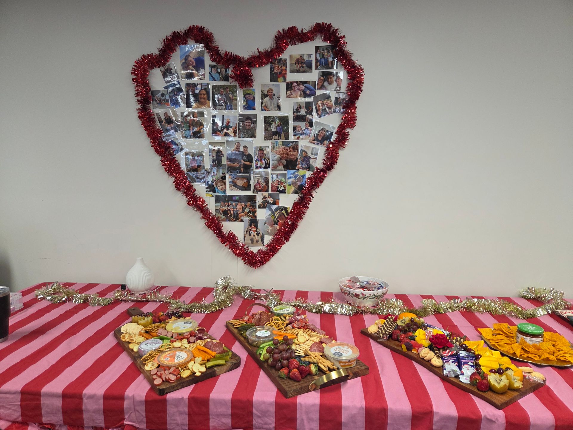 A table with three charcuterie boards on a red and white striped cloth, below a wall display of photos in a red heart — Advanced Therapy Mackay In Mackay, QLD 