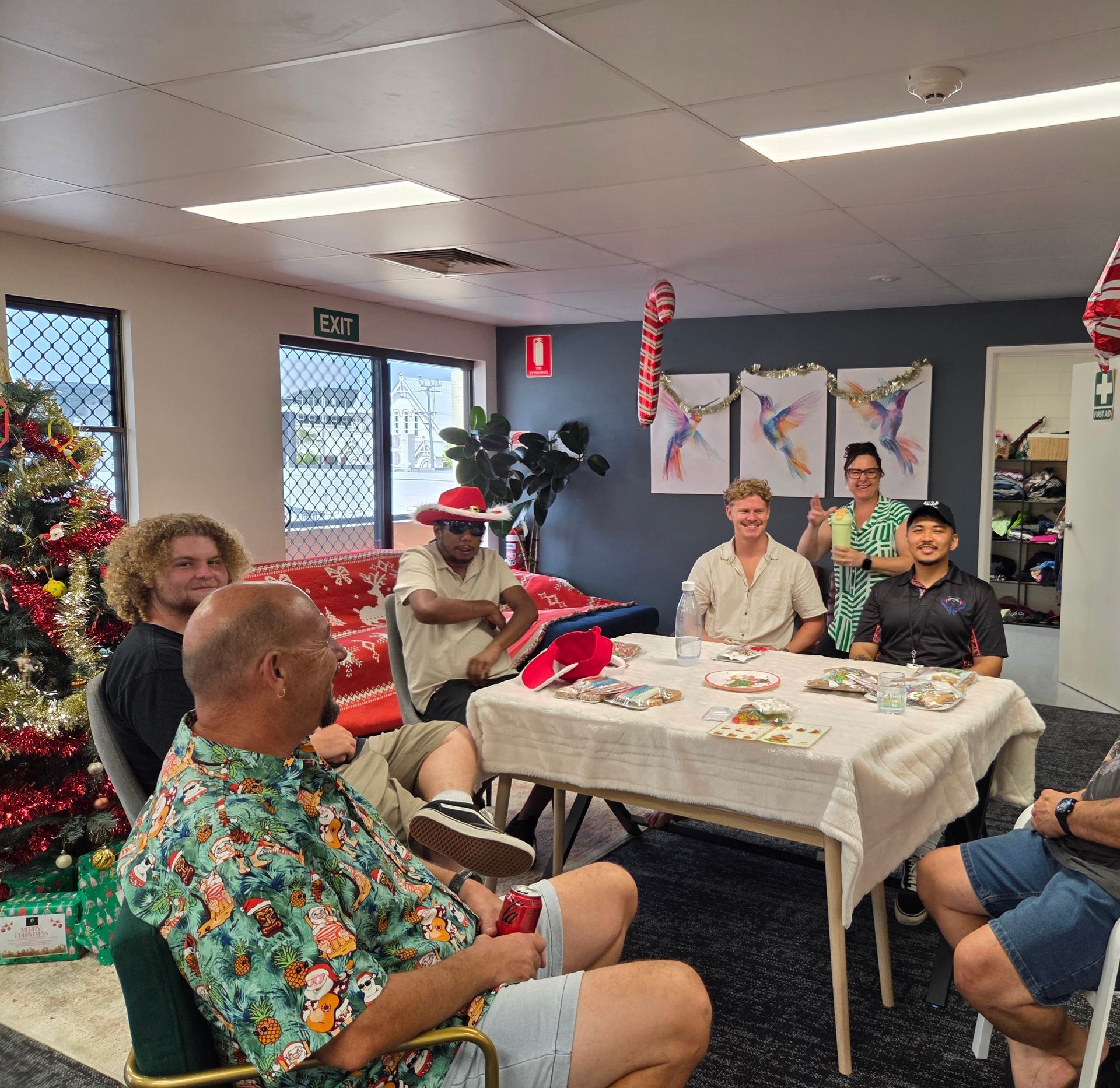 A group of people sitting around a table in a decorated room for a holiday meal, with a Christmas tree in the corner.