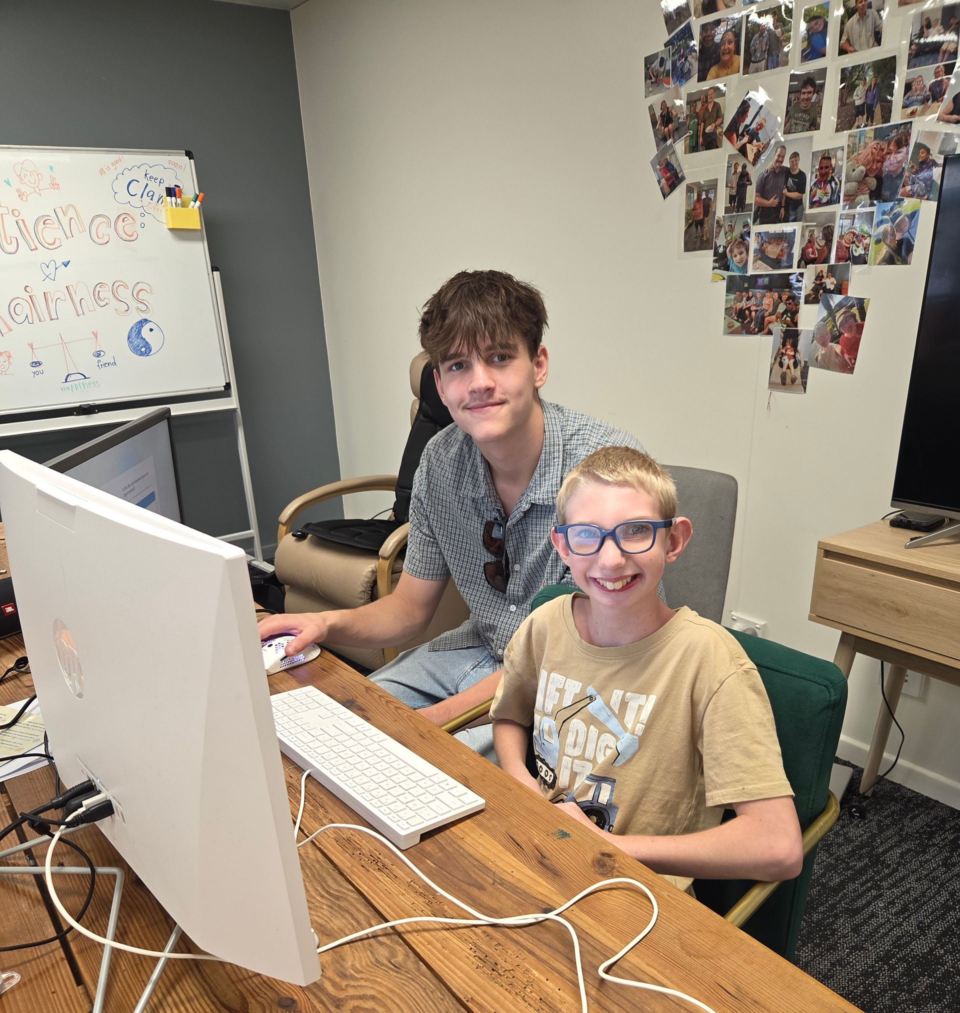 Two people sit at a wooden desk in an office, smiling while working together on a computer — Advanced Therapy Mackay In Mackay, QLD 