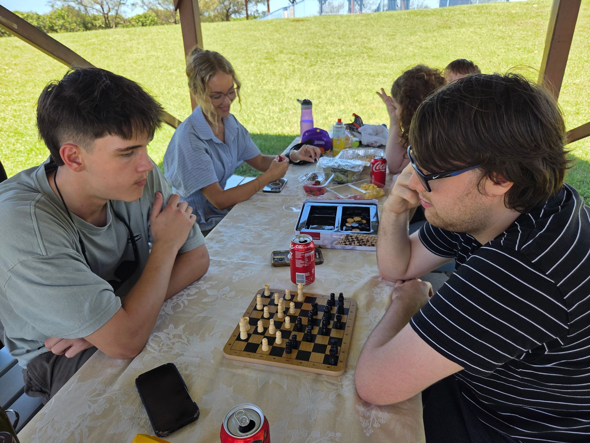 People Play Chess At An Outdoor Picnic Table Under A Wooden Pavilion — Advanced Therapy Mackay In Mackay, QLD 