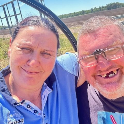 A Smiling Couple Poses For A Selfie Outdoors On A Sunny Day With A Field And Equipment In The Background — Advanced Therapy Mackay In Mackay, QLD 