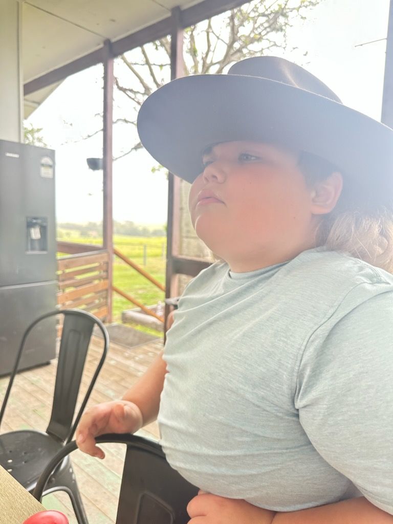 A person wearing a wide-brimmed hat sits at a table on an outdoor deck overlooking a grassy field — Advanced Therapy Mackay In Mackay, QLD 