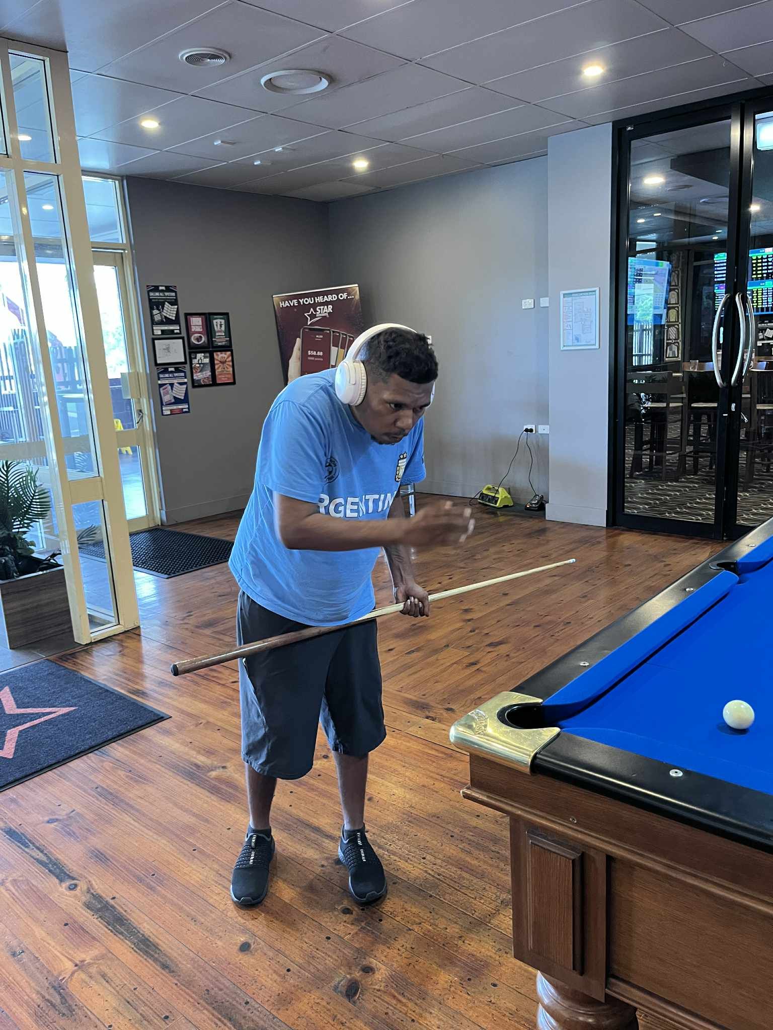 A Person In A Blue T-shirt And Shorts Holds A Pool Cue, Preparing To Take A Shot At A Blue-felt Pool Table — Advanced Therapy Mackay In Mackay, QLD 