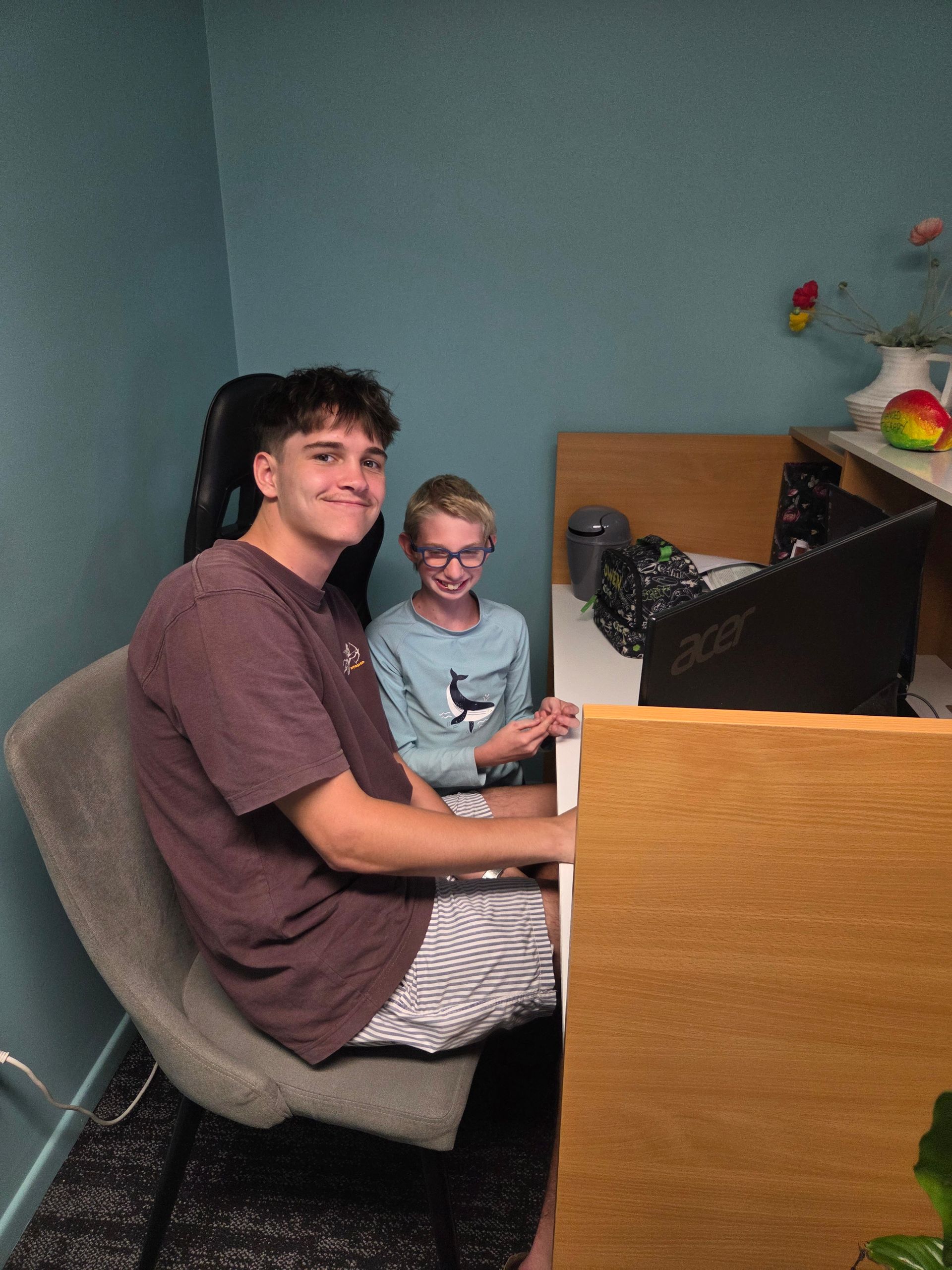 Two people sit at a desk in a blue-walled room, looking toward the camera; one faces forward, the other sits behind them — Advanced Therapy Mackay In Mackay, QLD 
