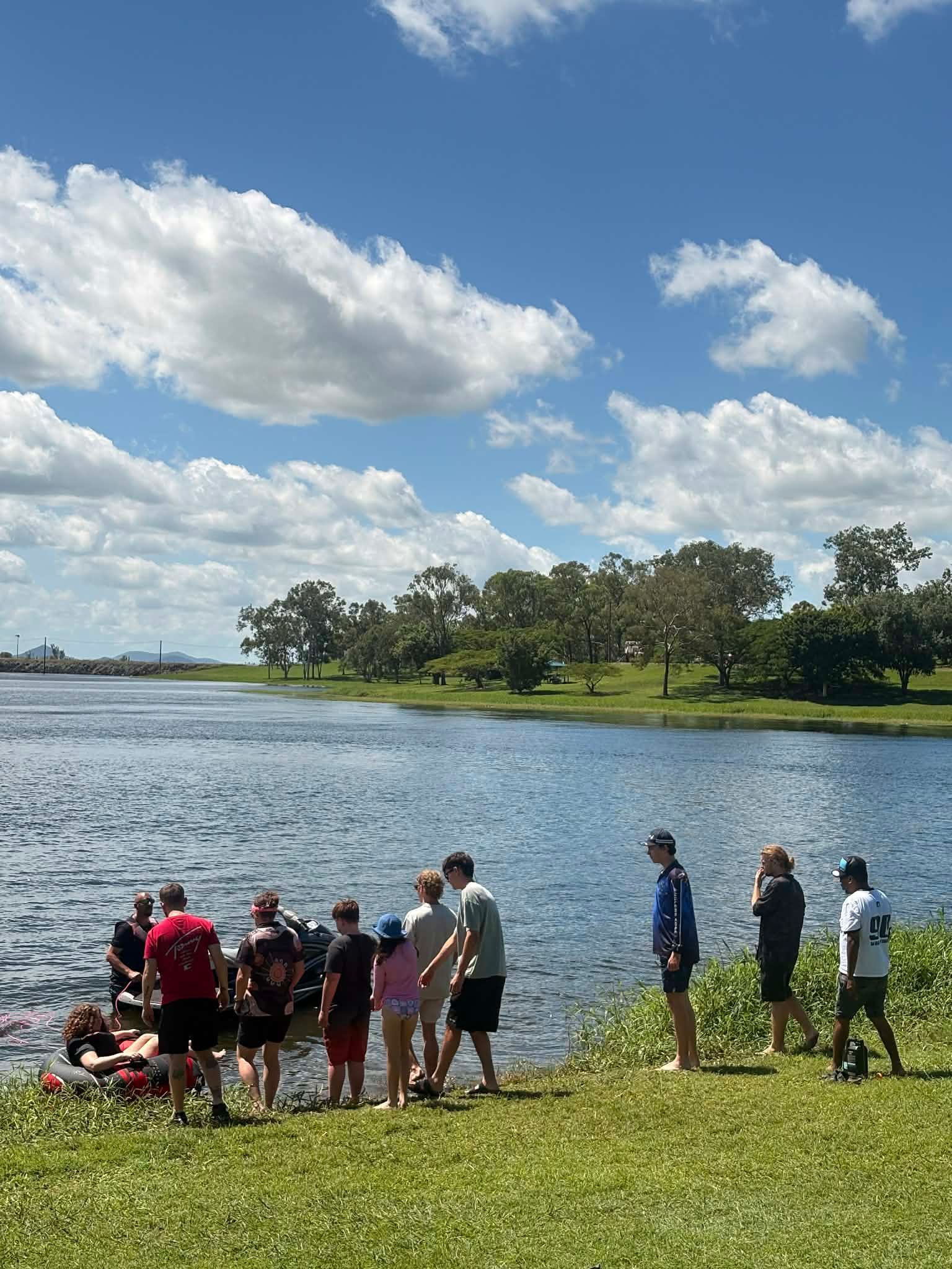 A Group Of People Standing On A Grassy Bank By A Lake Under A Blue, Cloudy Sky — Advanced Therapy Mackay In Mackay, QLD 