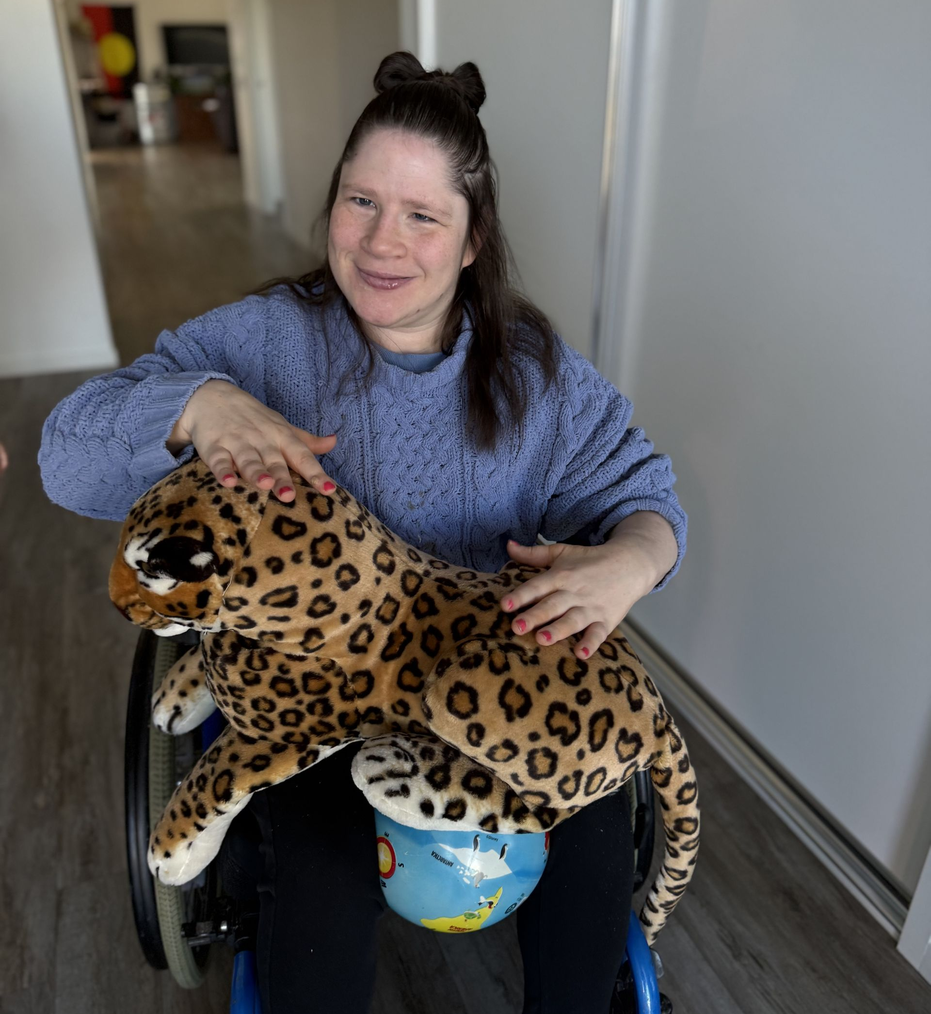 A Person In A Wheelchair Smiles While Holding And Petting A Large Plush Leopard Toy — Advanced Therapy Mackay In Mackay, QLD 