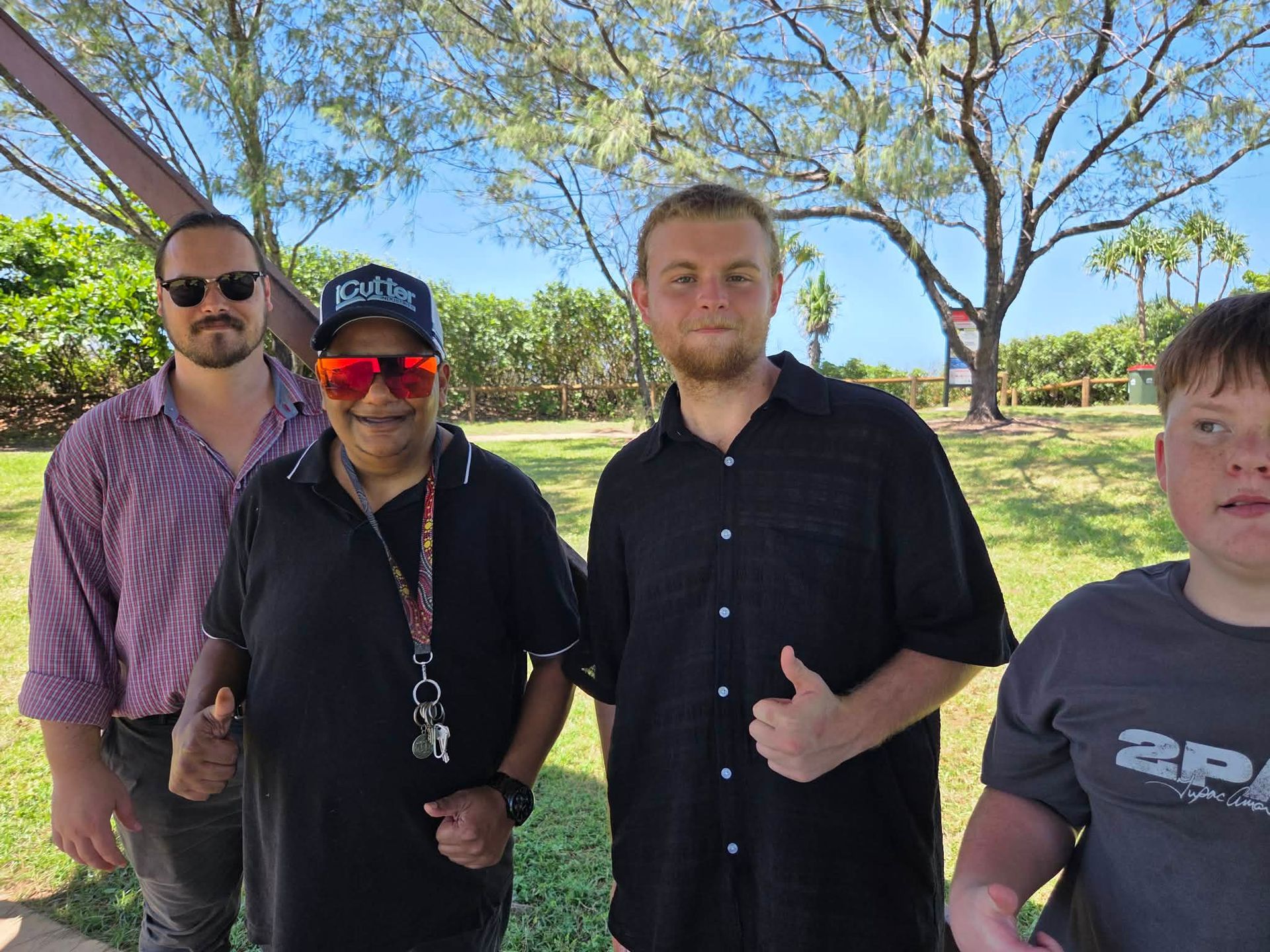 Four People Pose Outdoors On A Sunny Day In A Park, With Trees In The Background And Two Individuals Giving Thumbs Up — Advanced Therapy Mackay In Mackay, QLD 