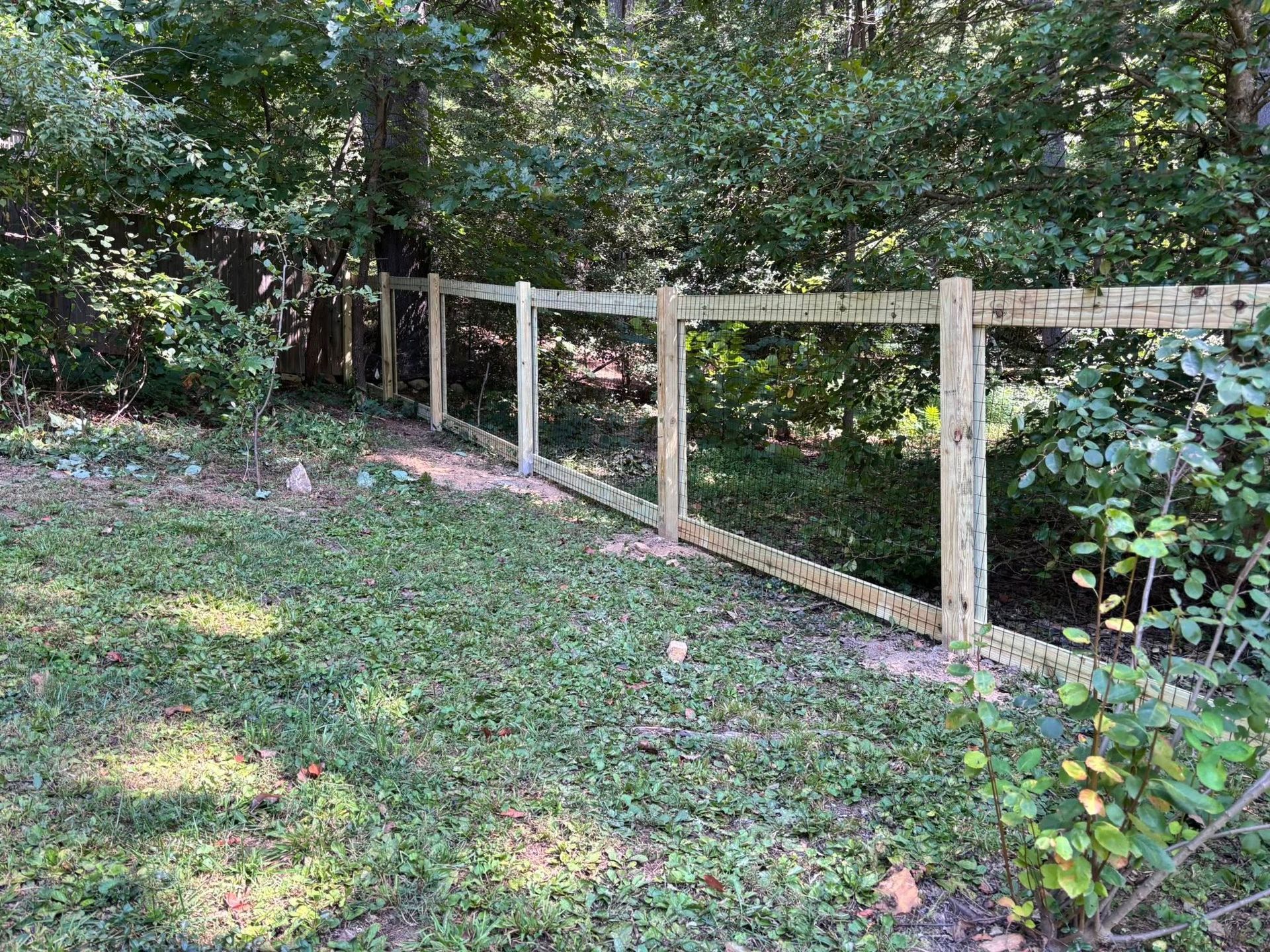 A newly installed wooden post-and-rail fence standing in a grassy backyard bordering a wooded area.