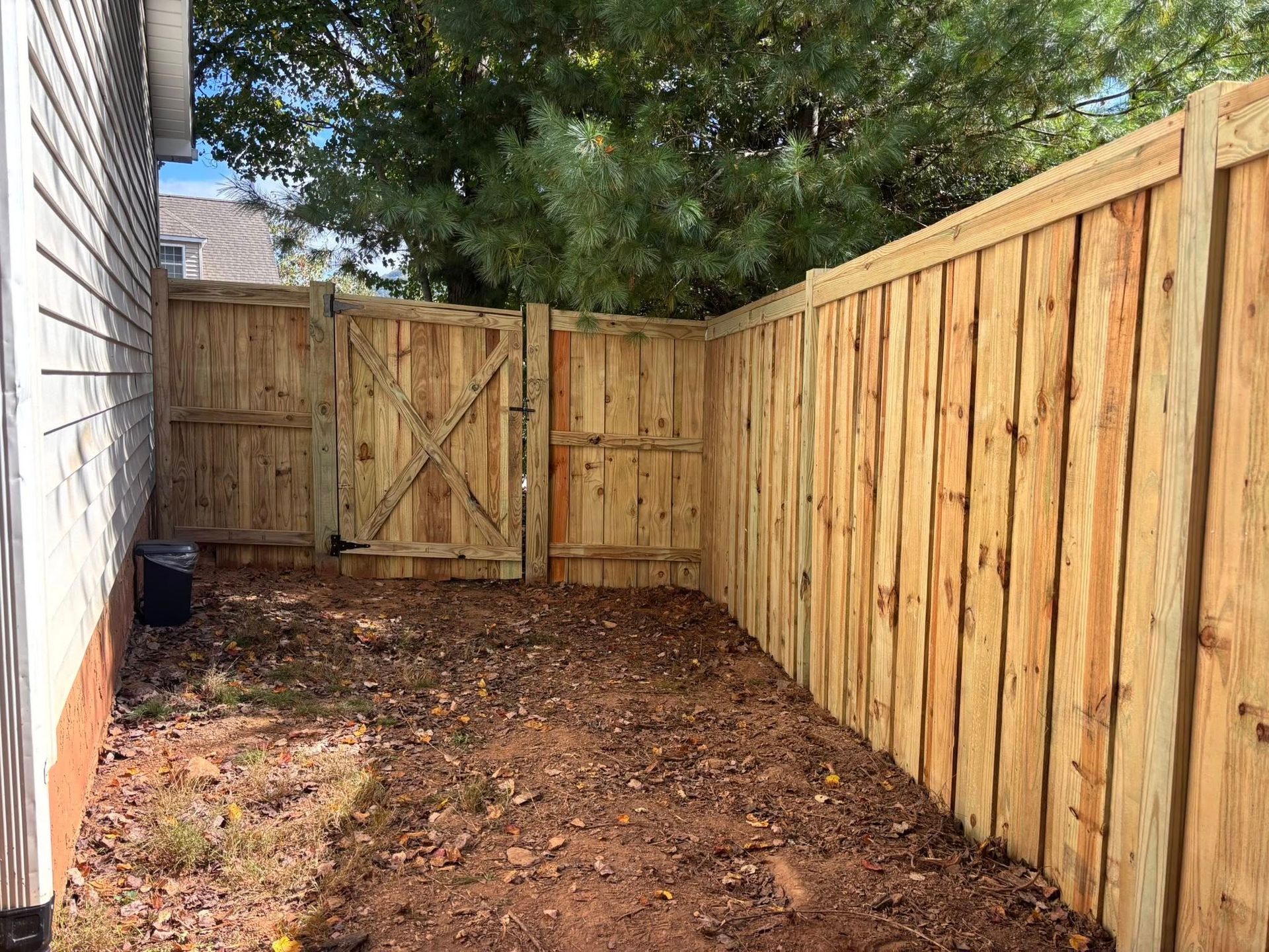 A new wooden privacy fence encloses a backyard corner, featuring a hinged gate with a cross-brace design.