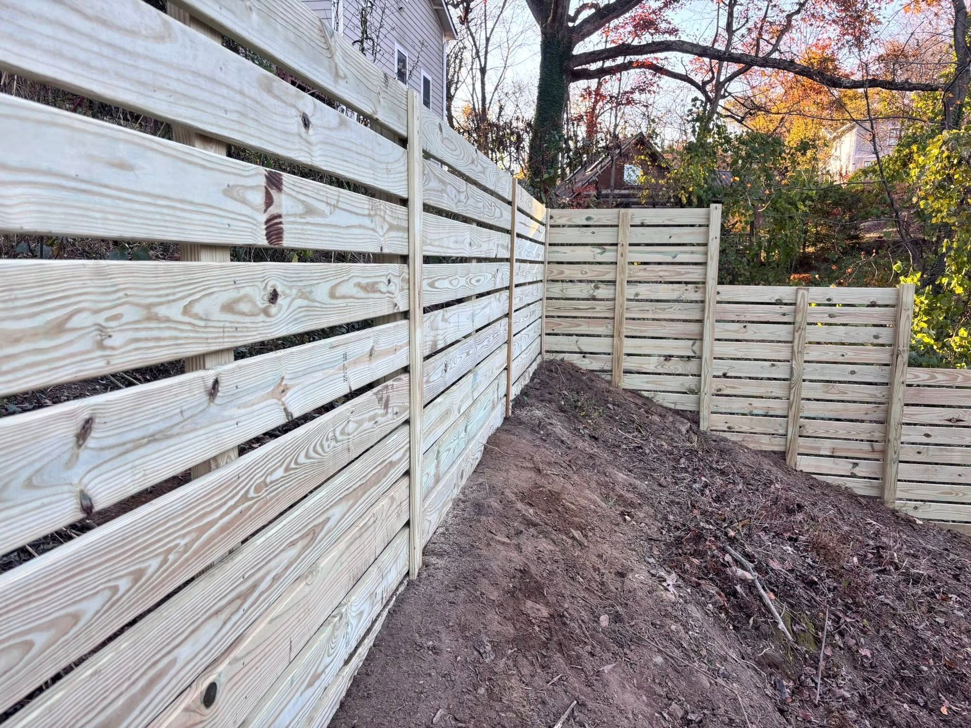 A modern horizontal wood fence built in a tiered, stepped design along a sloped dirt hillside.