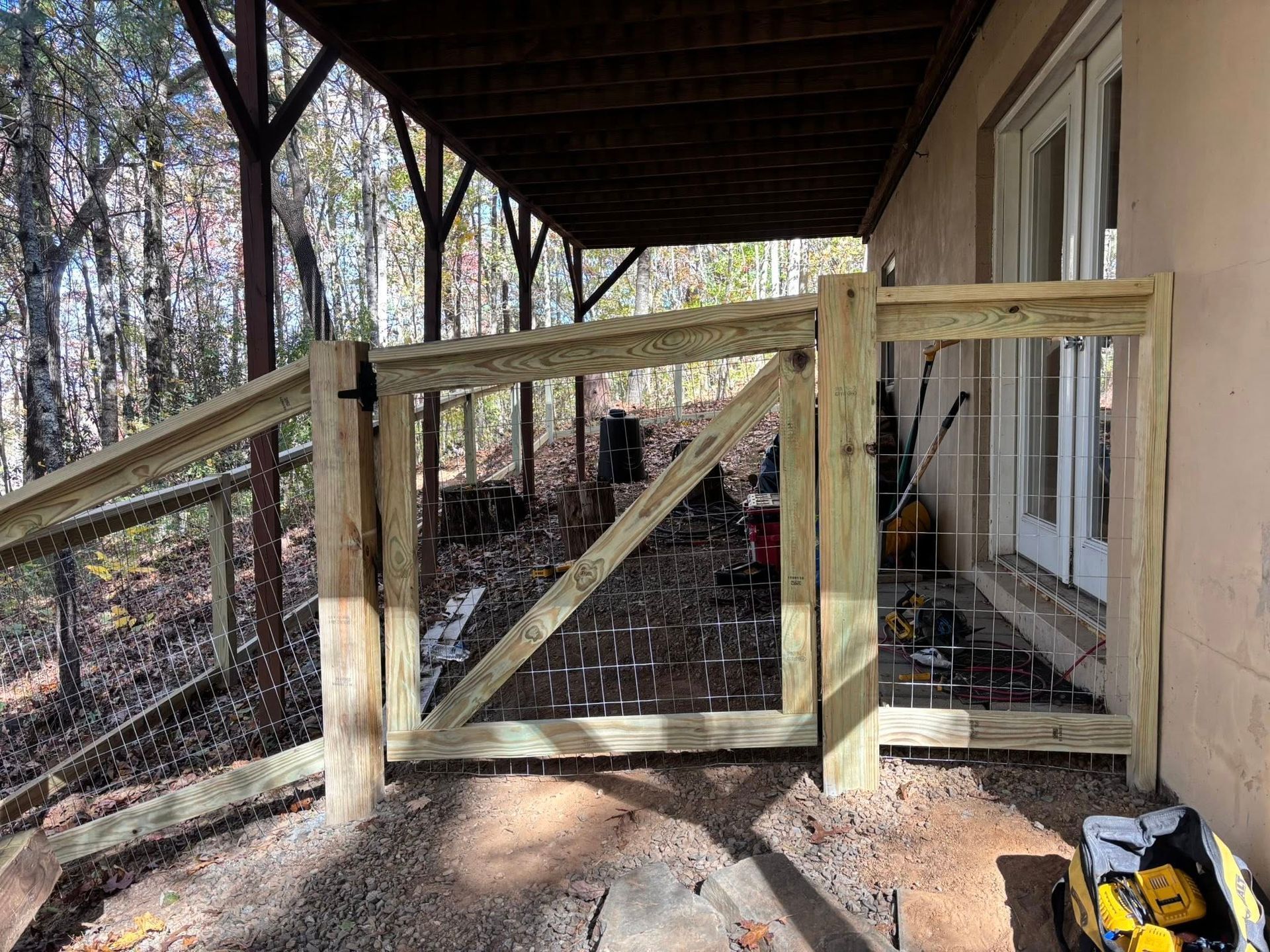 A wooden gate under a porch attached to the side of a house, overlooking a wooded area.