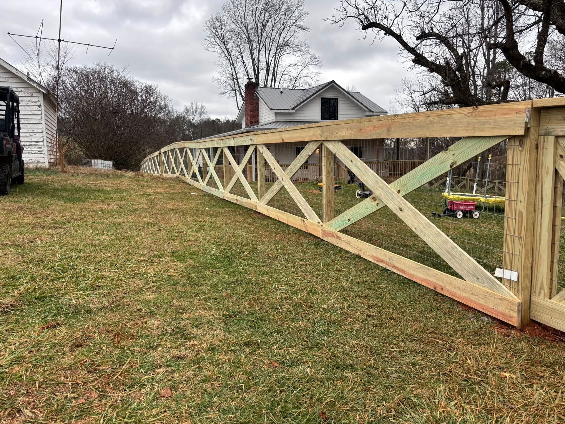 A long, wooden fence with an X-pattern lattice design running through a grassy yard in front of a house.