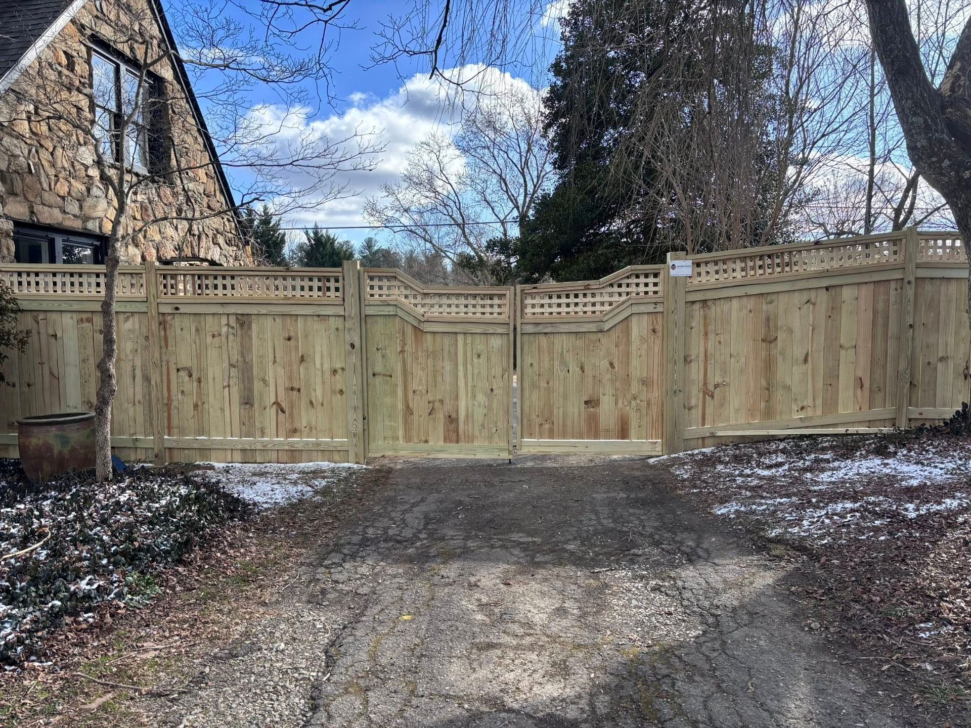 A large, wooden privacy gate with a decorative lattice top spans a gravel driveway in front of a stone house.