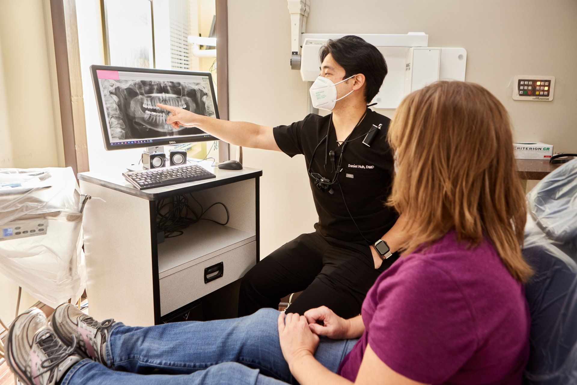 Dentist pointing to a dental x-ray on a computer screen, explaining to a seated patient.