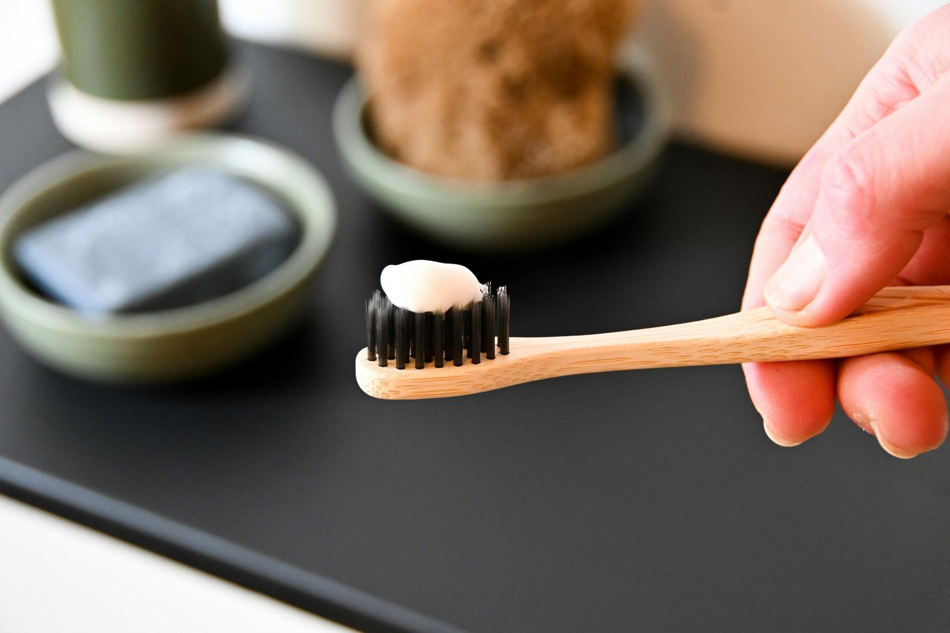 A person is holding a wooden toothbrush with toothpaste on it.