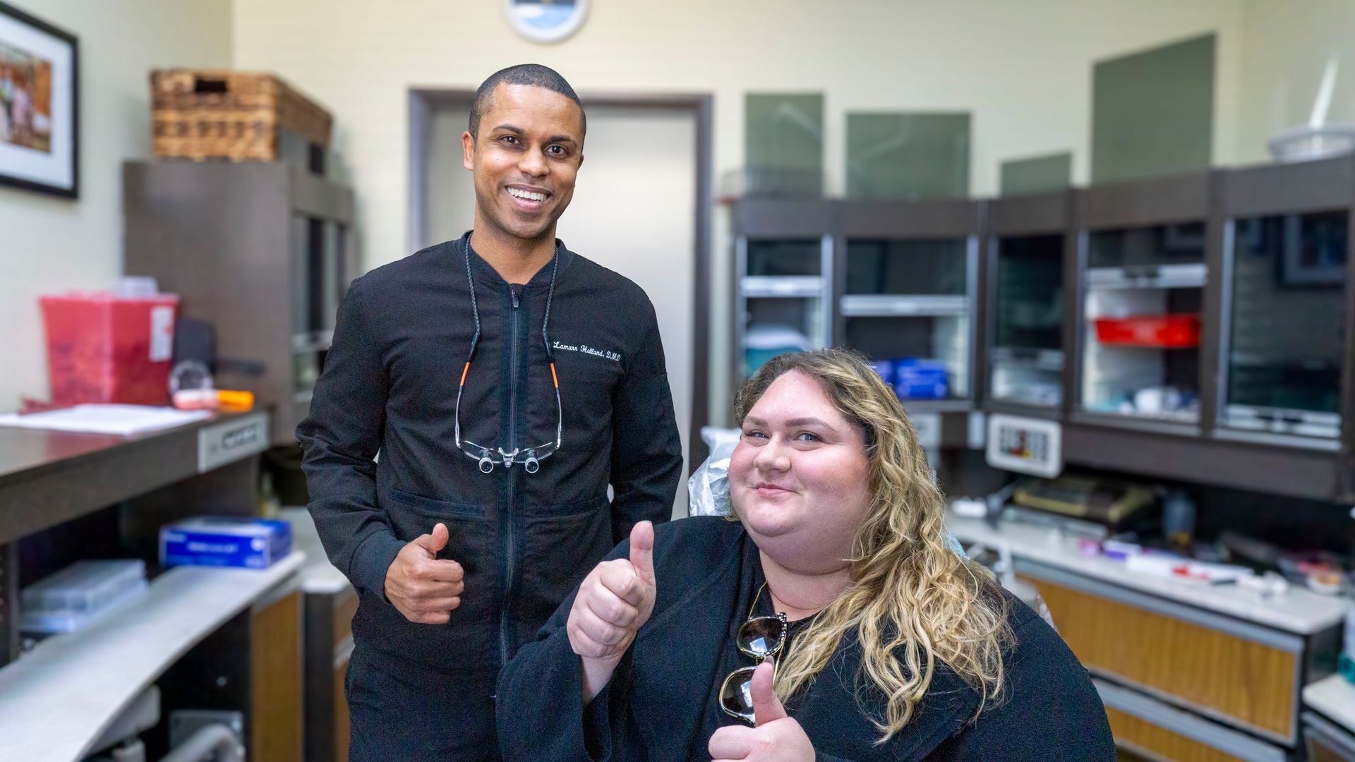 A man and a woman are giving a thumbs up in a dental office.