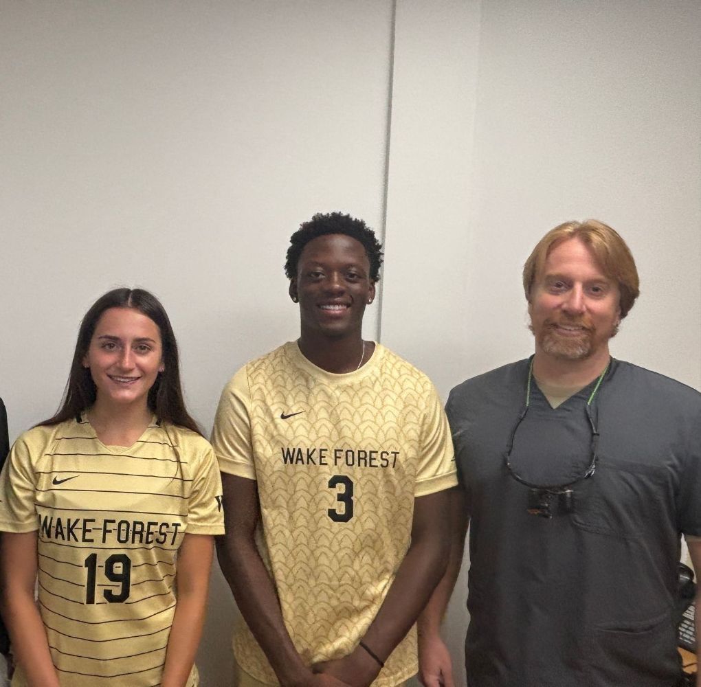 Three people posing for a picture with one wearing a wake forest jersey