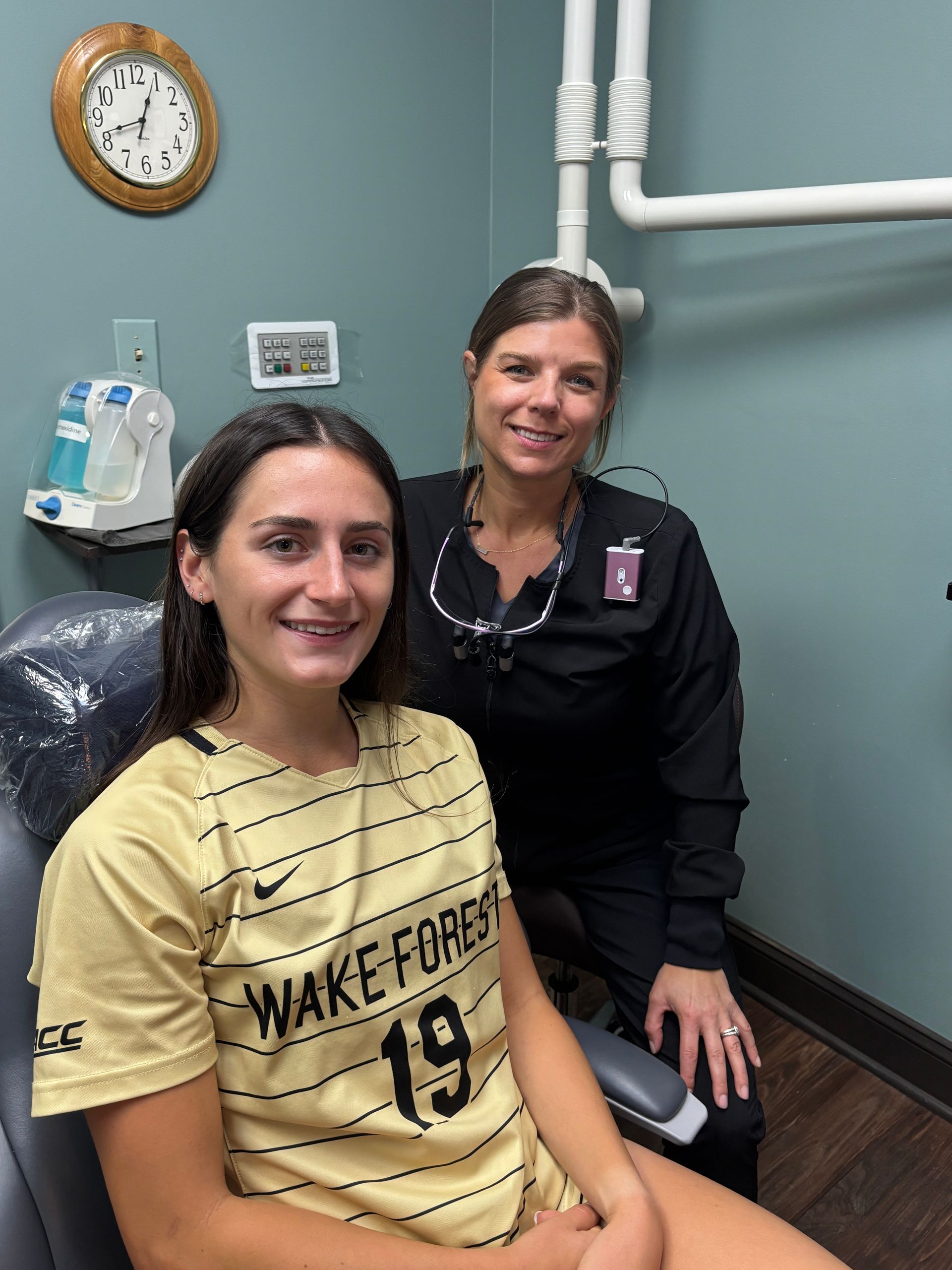 A woman wearing a wake forest jersey sits in a dental chair