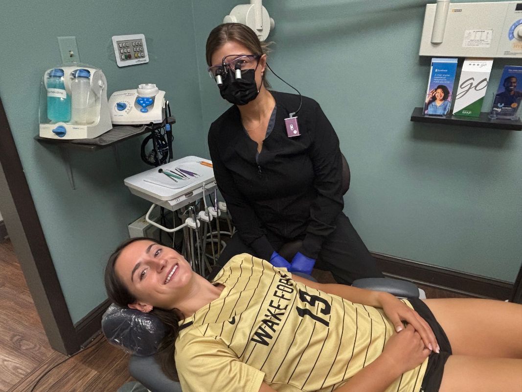 A woman is laying in a dental chair with a dentist standing behind her.