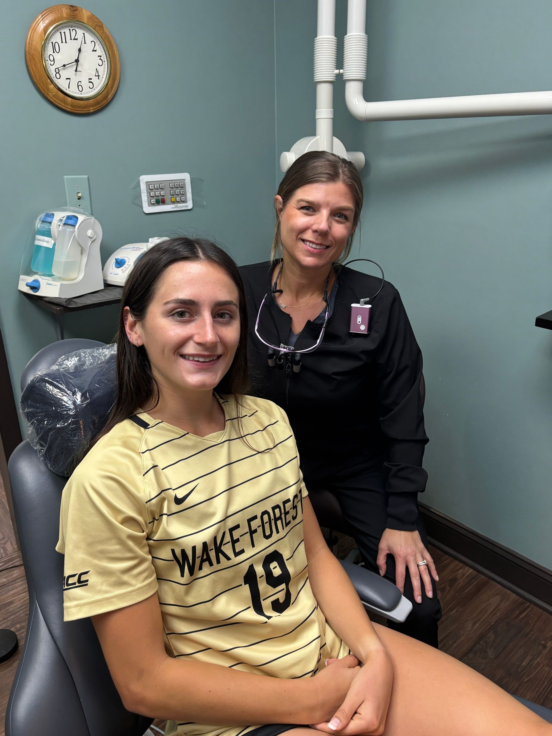 A woman is sitting in a dental chair next to a dentist.