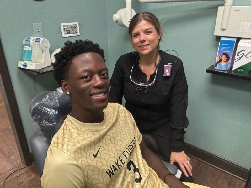 A man in a wake forest shirt sits in a dental chair next to a woman