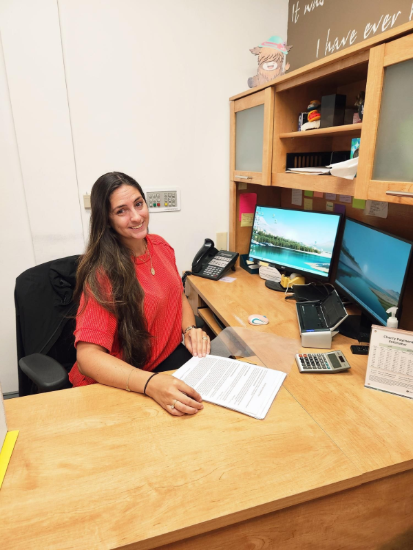 Woman in red shirt smiling at a desk with two monitors.