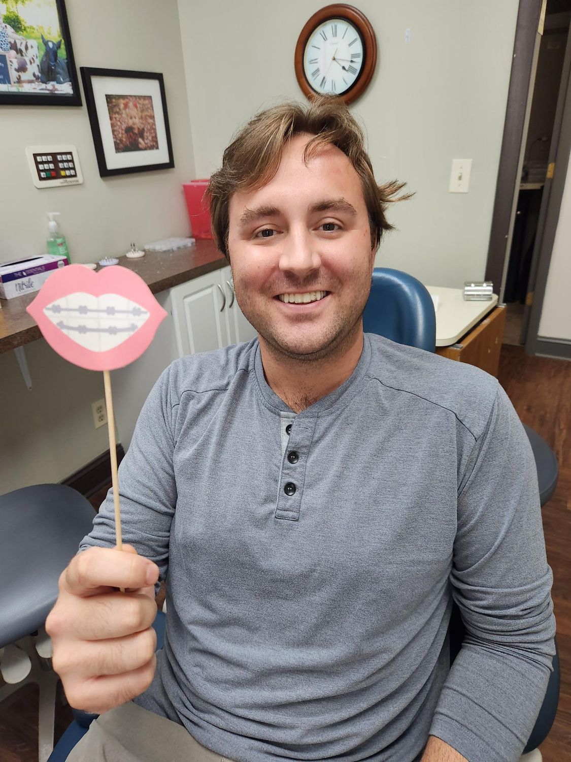 Man smiling, holding a prop of braces, in a dentist's office.