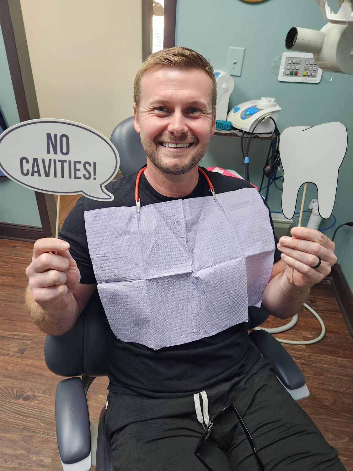 Man in dental chair smiles, holding 