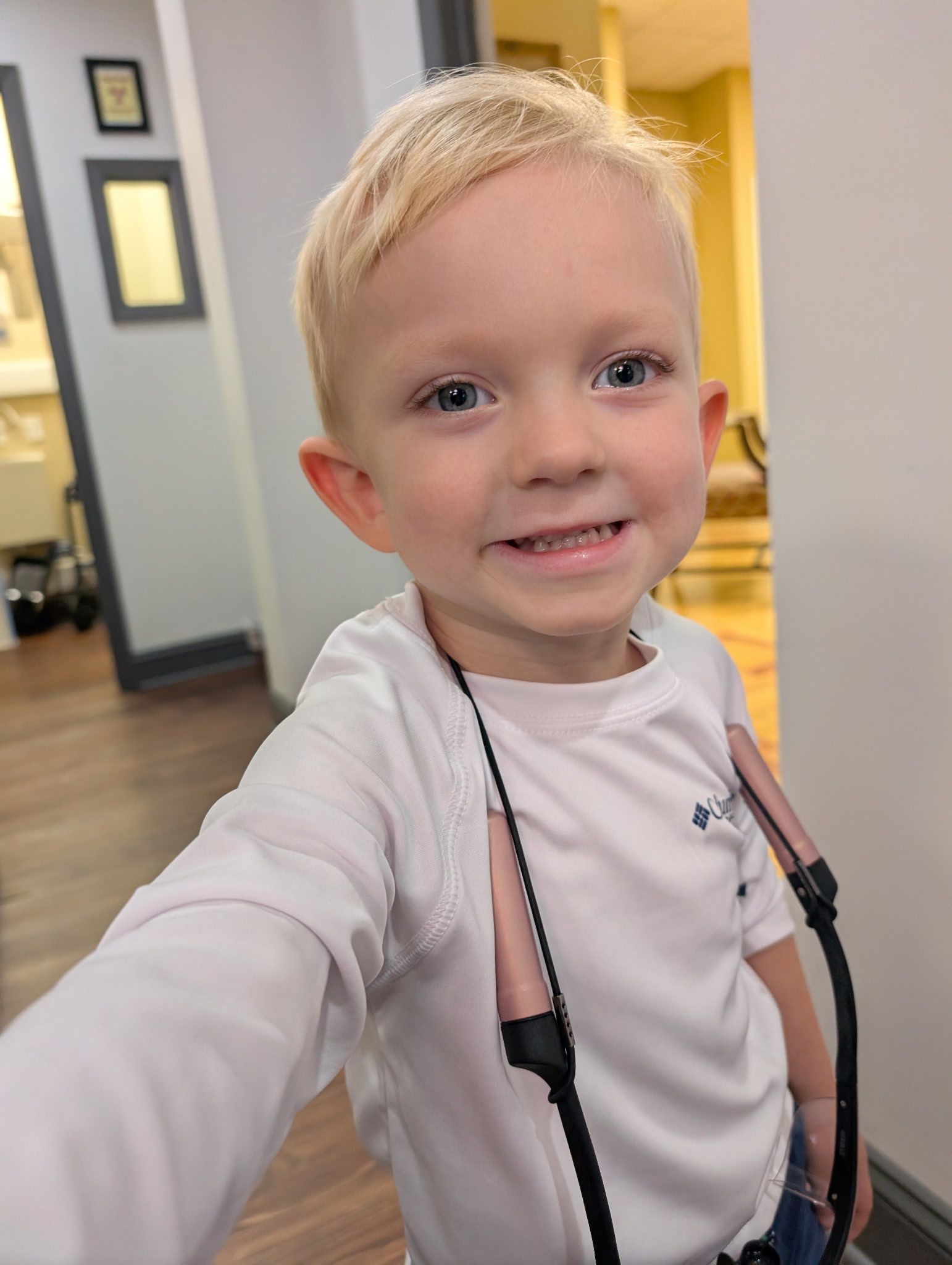Blonde-haired boy smiling, wearing white shirt with a jump rope around his neck.