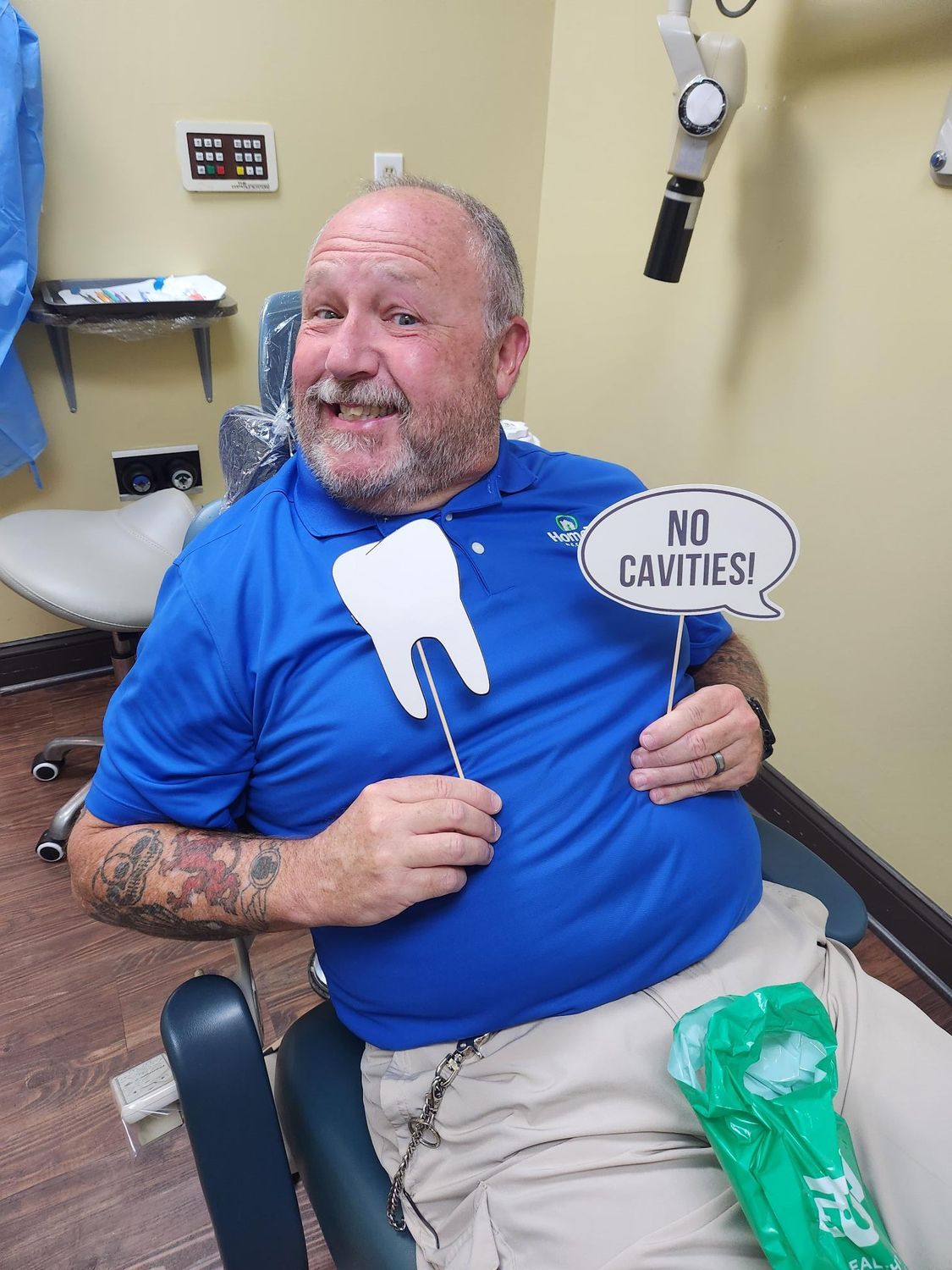 Man in blue shirt at dentist, holding tooth cutout and 