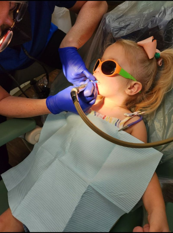 A little girl is sitting in a dental chair getting her teeth examined by a dentist.