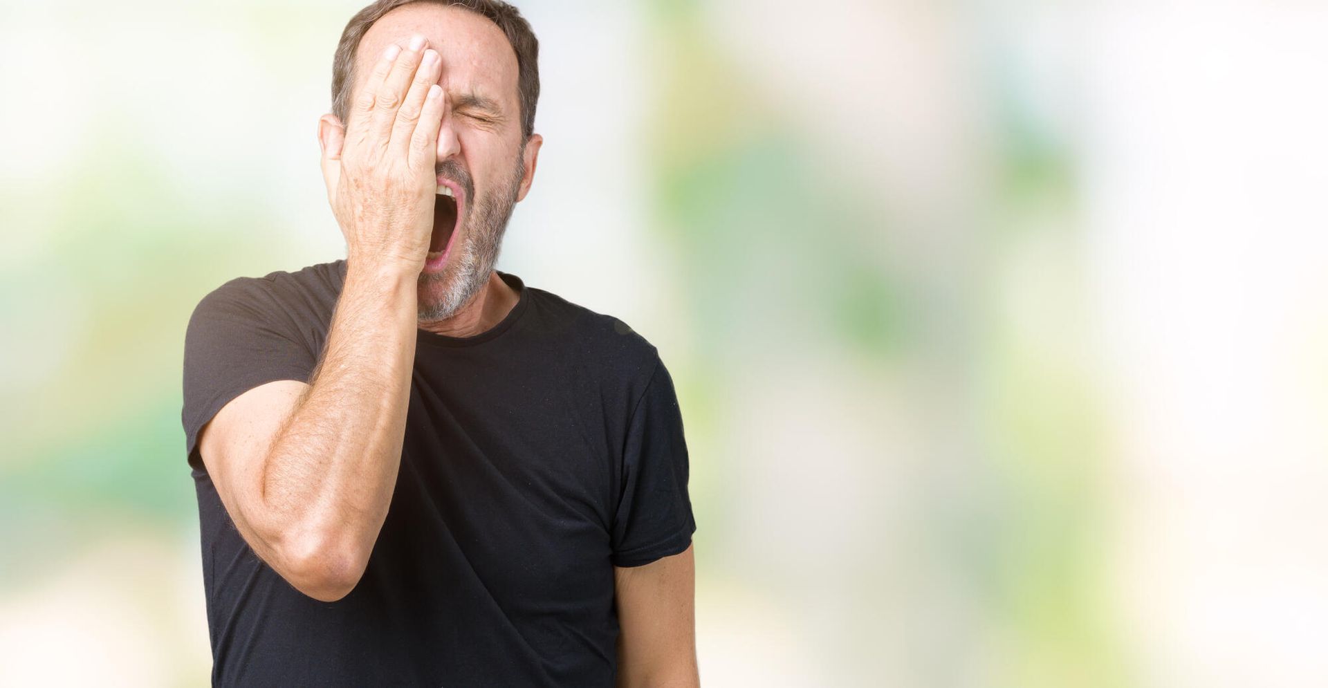 A man is covering his face with his hand and yawning.