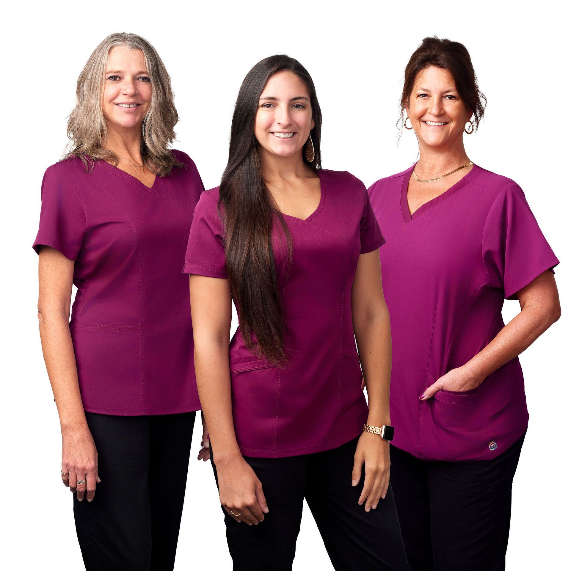 Three women wearing purple scrub tops and black pants are posing for a picture.