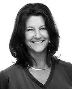 A black and white photo of a smiling woman wearing a scrub top.