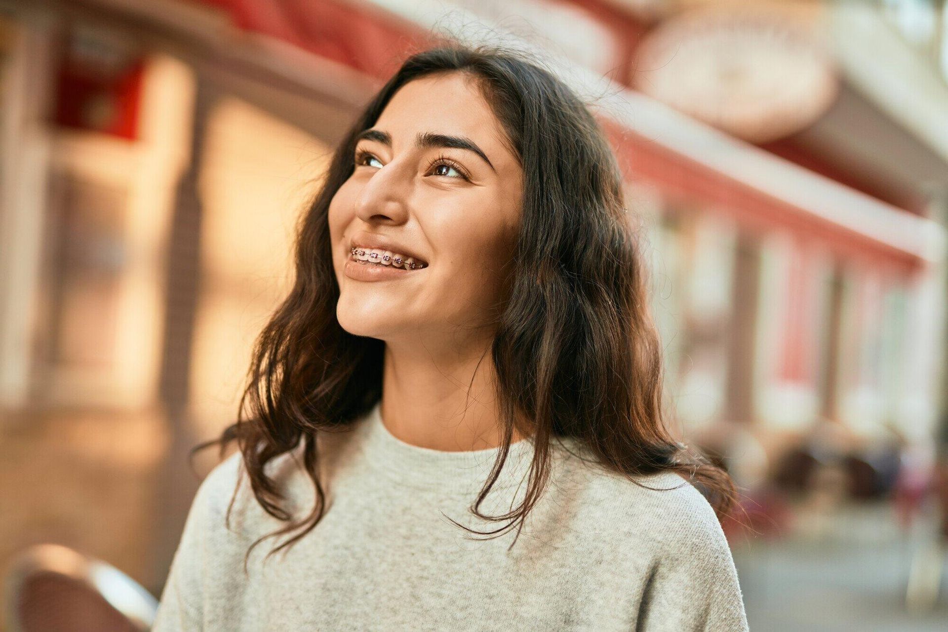 A young woman with braces on her teeth is smiling and looking up.