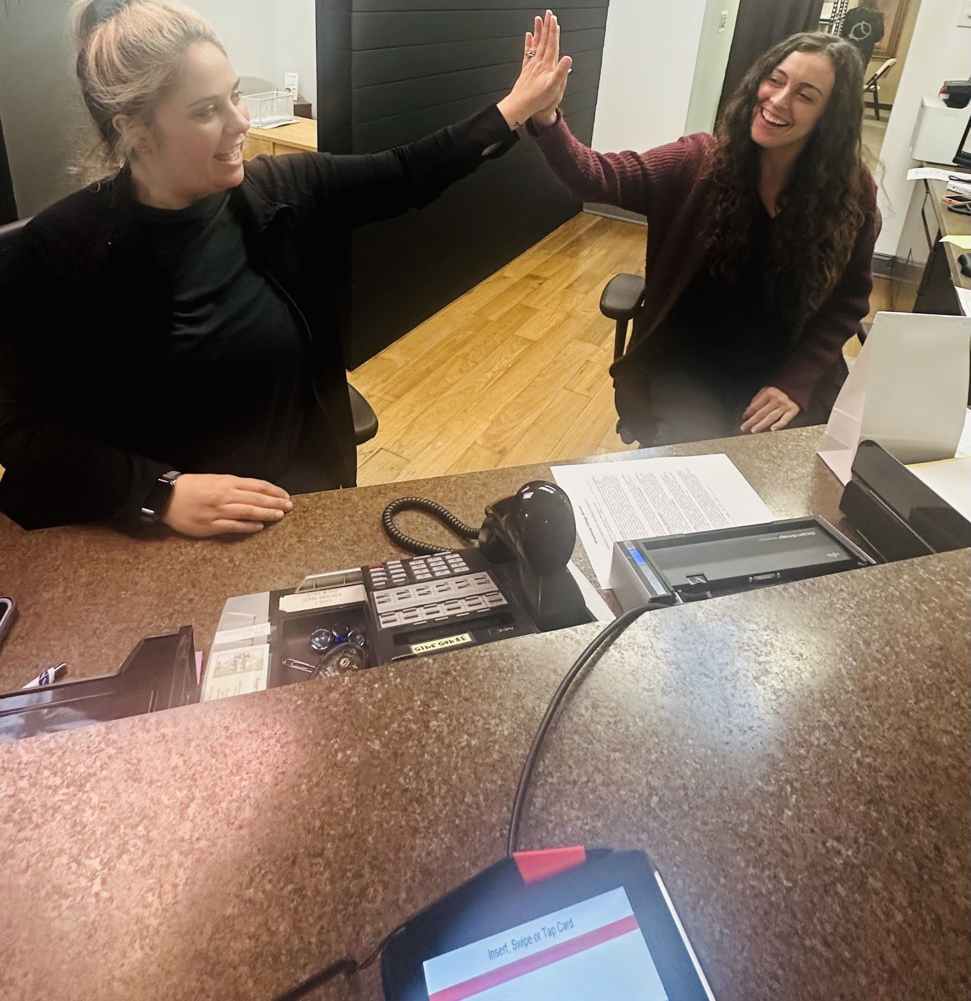 Two women are giving each other a high five while sitting at a counter.