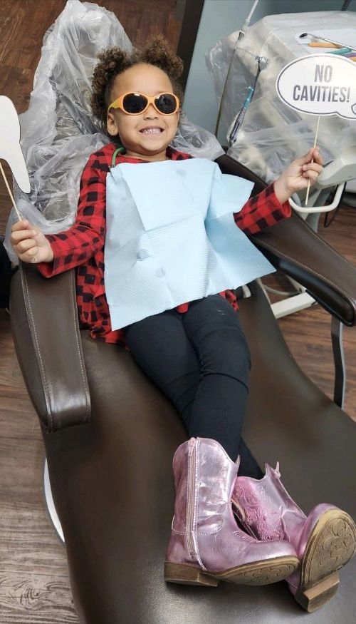 Una niña está sentada en una silla dental y lleva gafas de sol.