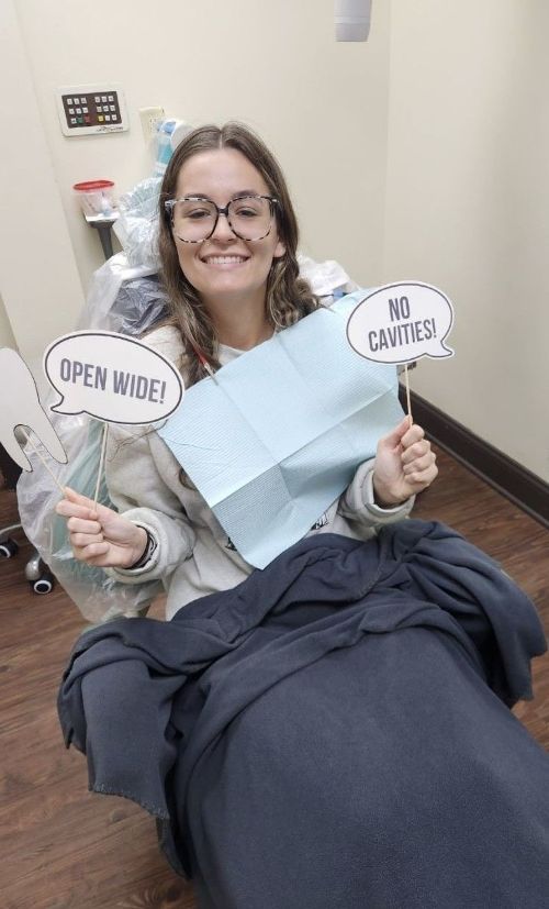Una mujer está sentada en una silla dental sosteniendo un cartel.