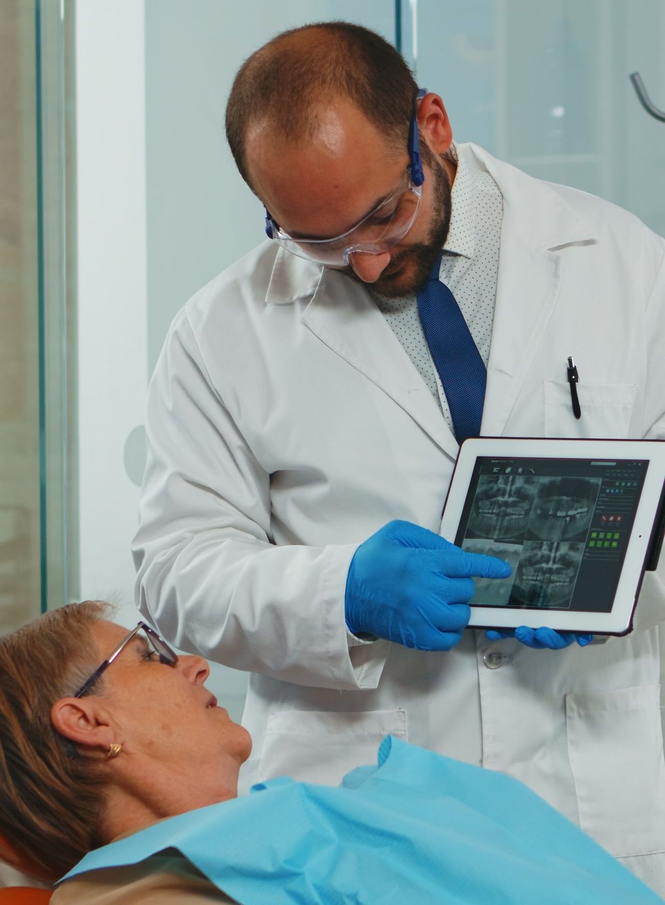 A dentist is looking at an x-ray of a patient 's teeth on a tablet.