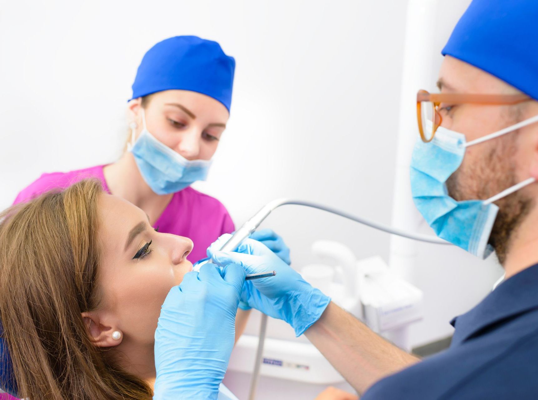 A woman is sitting in a dental chair while a dentist examines her teeth.