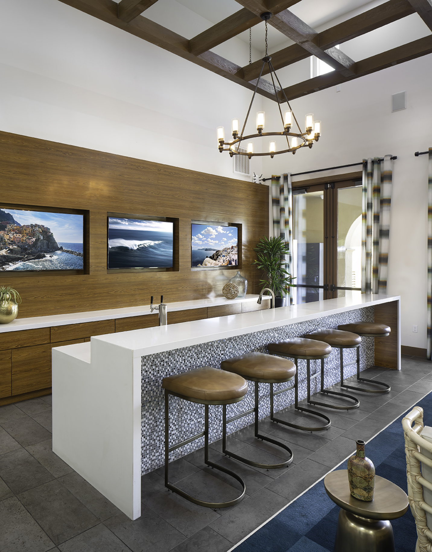 A kitchen with a long counter and stools and a chandelier hanging from the ceiling.