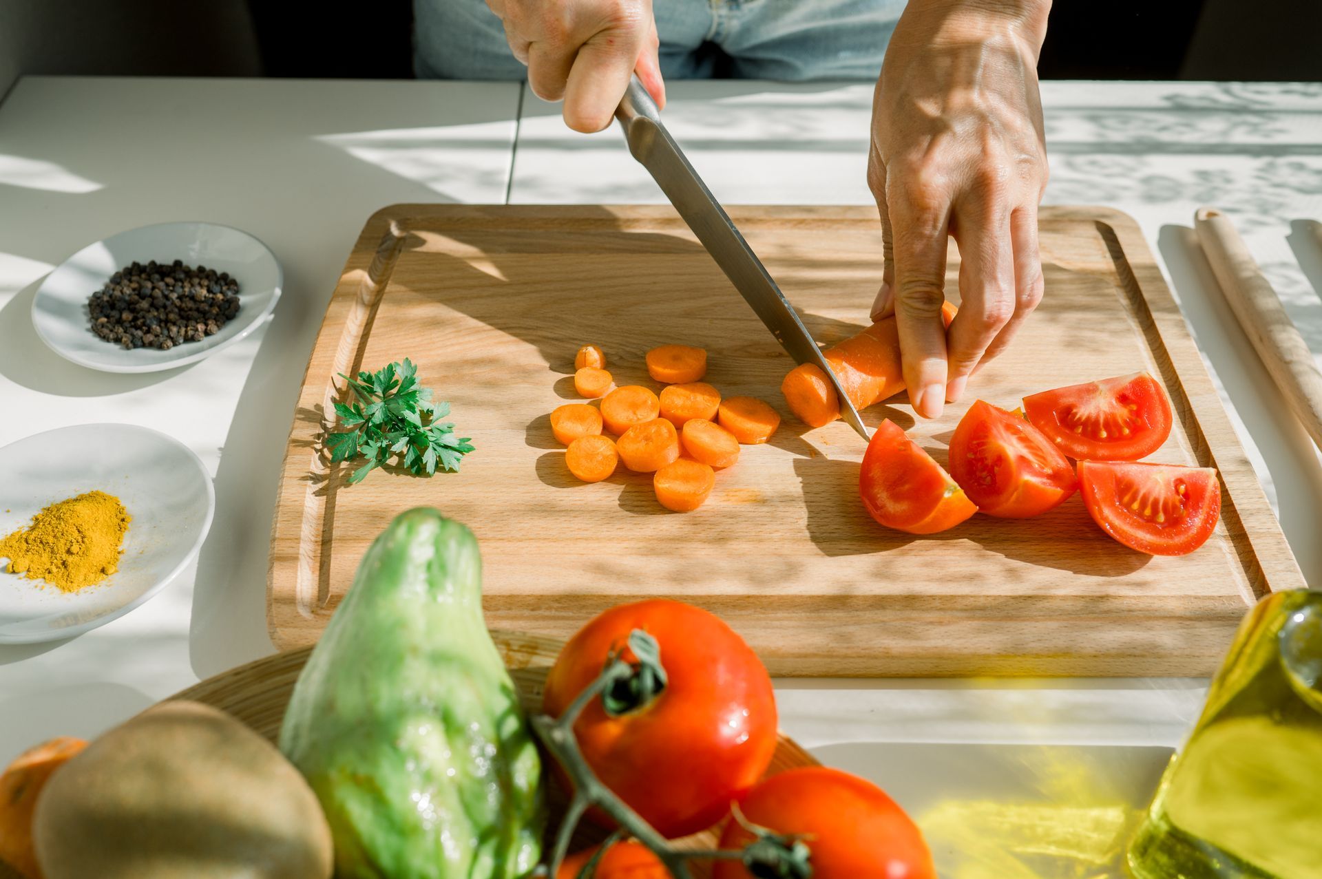 Person chopping vegetables on a wooden cutting board, with tomatoes, carrots, and spices visible.