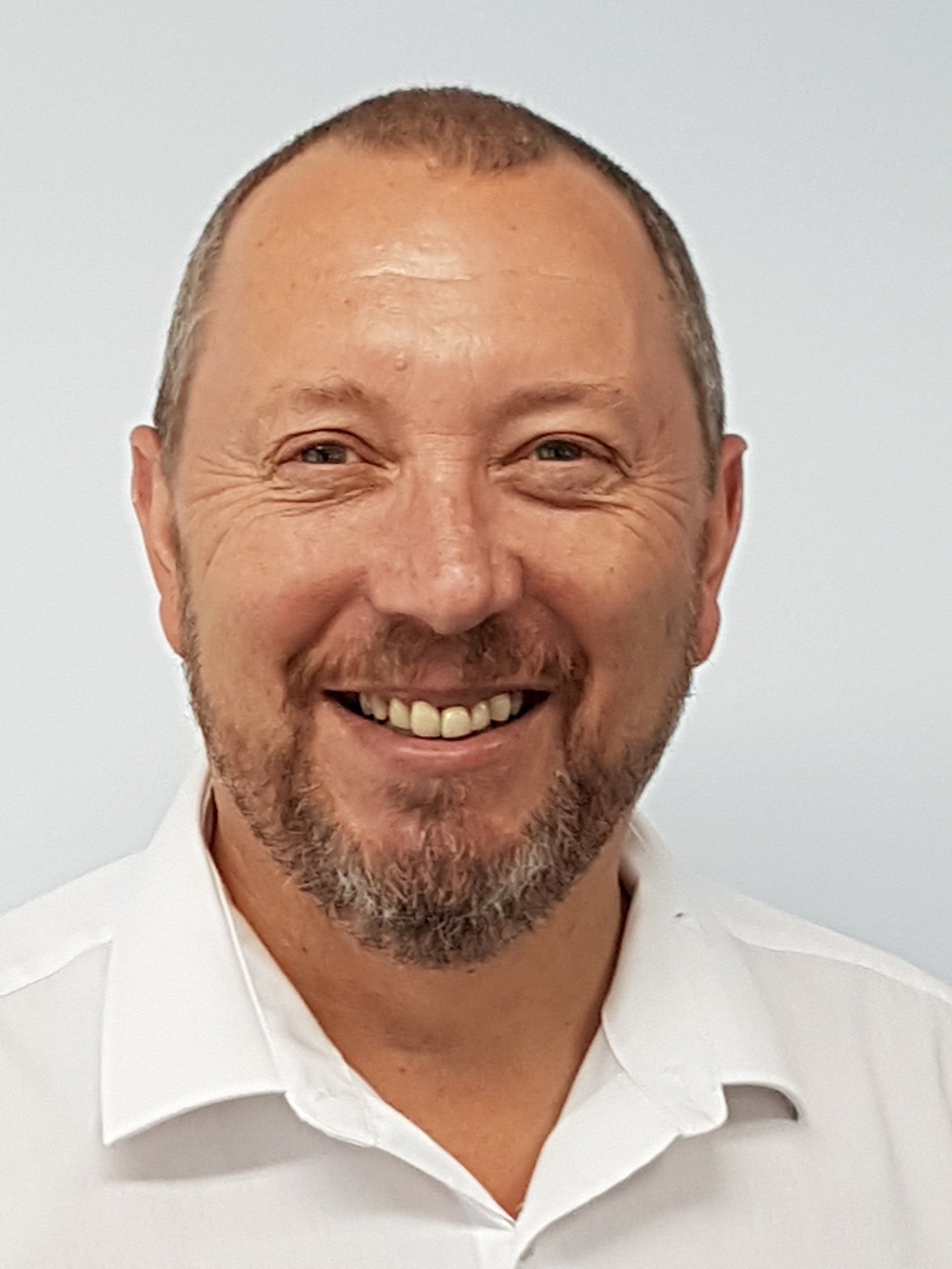 A man with a beard is smiling for the camera while wearing a white shirt.