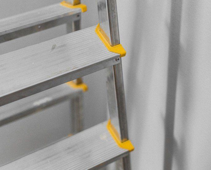 A close up of a ladder with yellow handles against a white wall.