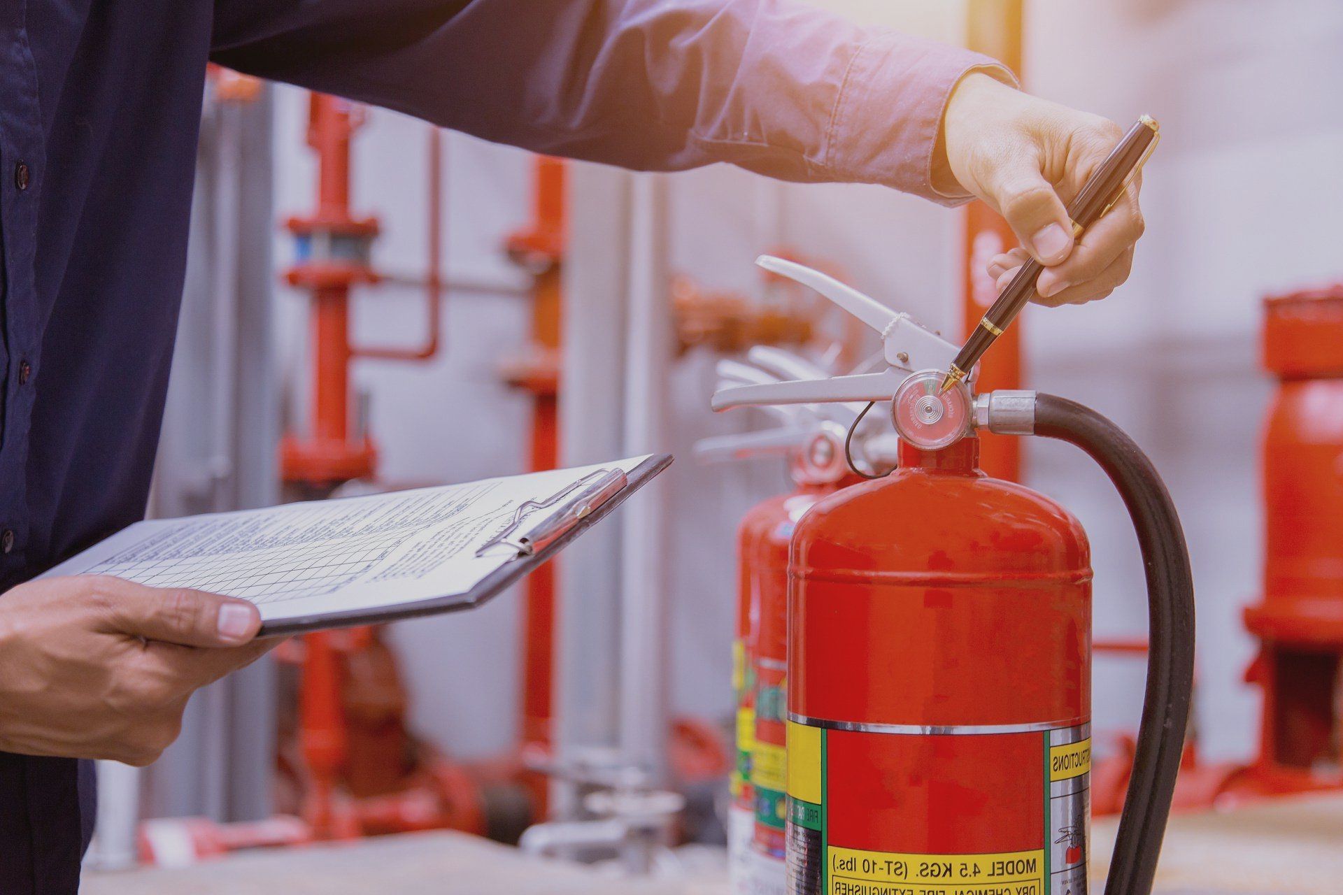 A man is checking a fire extinguisher while holding a clipboard.