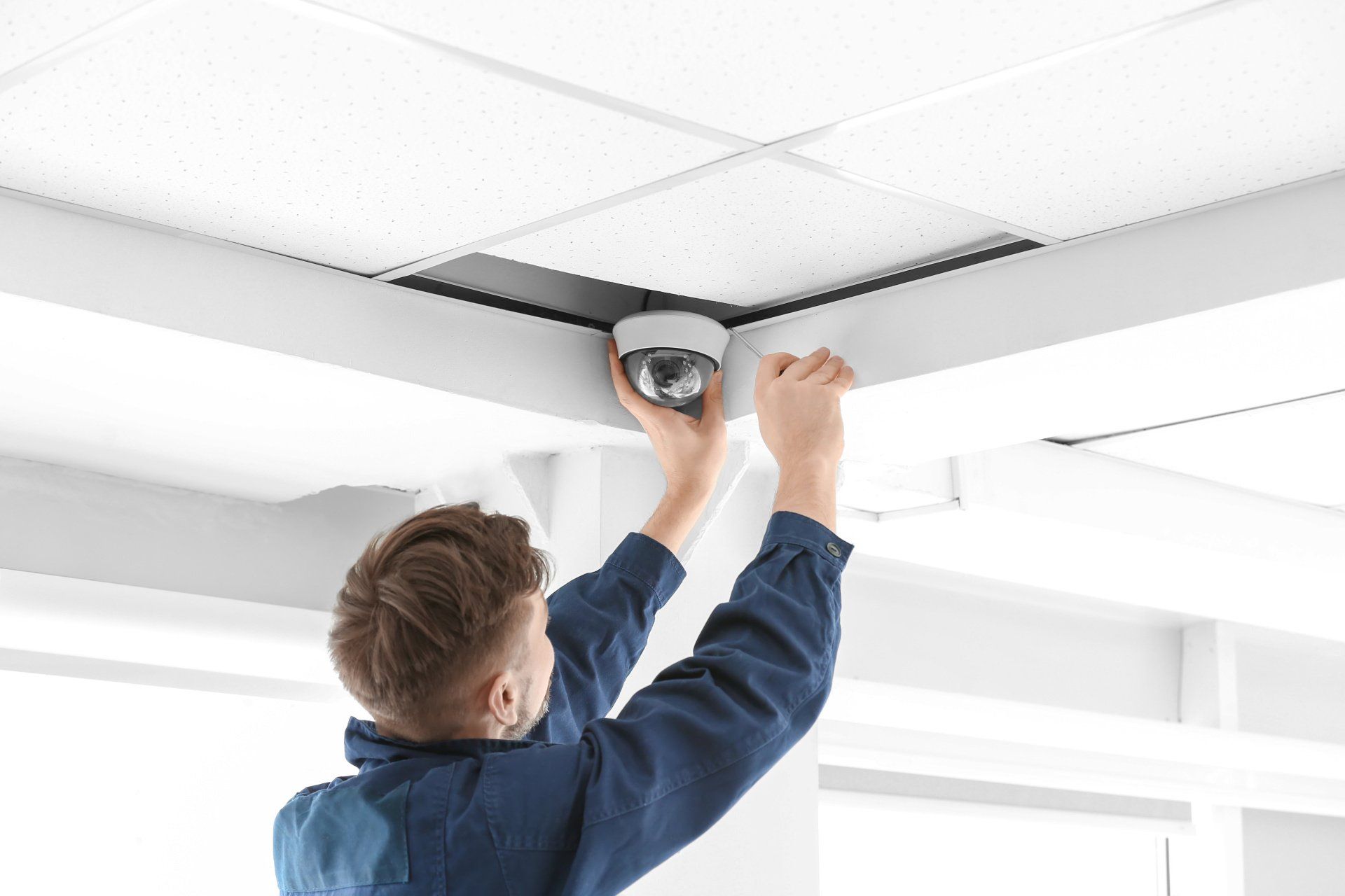 A man is installing a security camera on the ceiling.